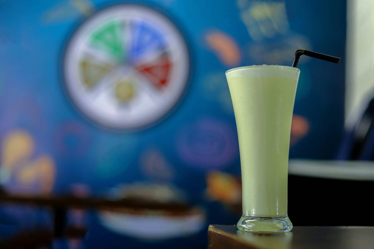 A vibrant green smoothie in a glass next to fresh spinach, kale, and spirulina powder labeled health drink organic smoothy super green
